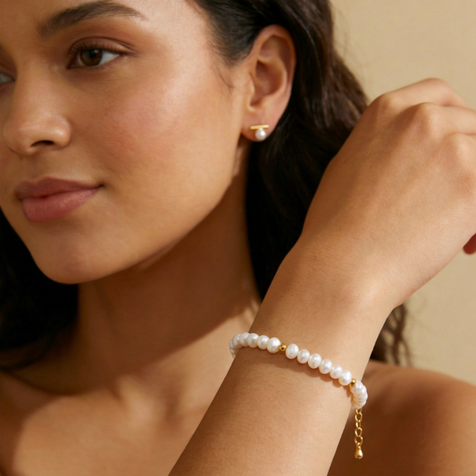 Woman wearing a pearl bracelet and earring on a neutral background