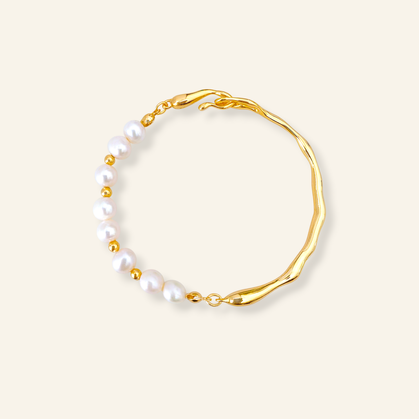 A gold-toned bracelet featuring a wavy, organic-shaped band and a row of white freshwater pearls separated by small gold beads, set against a solid cream background.
