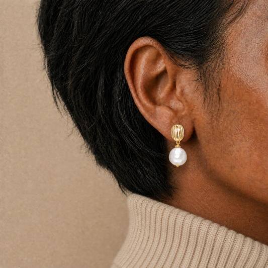 Close-up of an ear wearing a gold earring with a pearl drop against a beige background