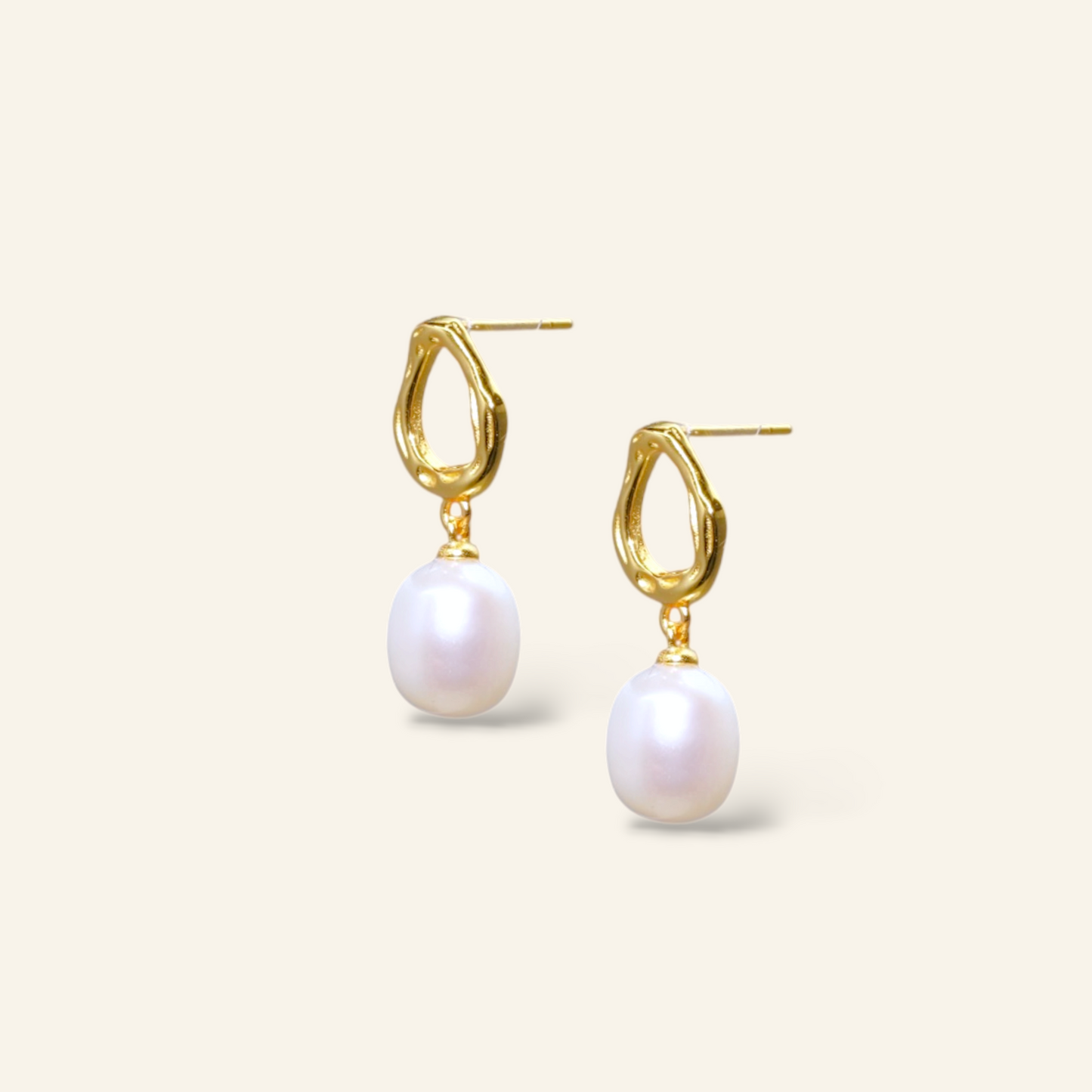 Gold earrings with white pearls on a light beige background