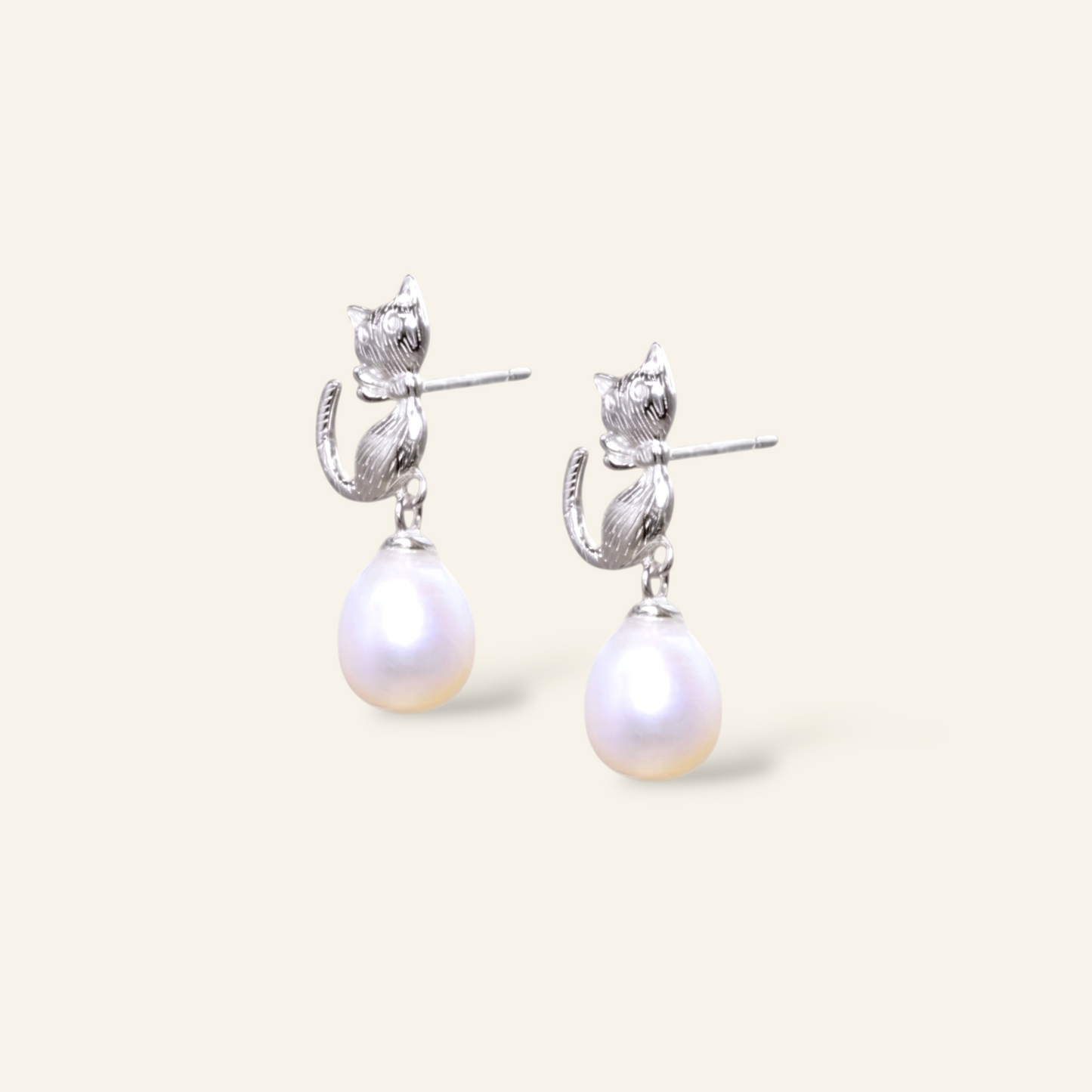 Pair of pearl earrings with silver cat-shaped clasps on a light beige background