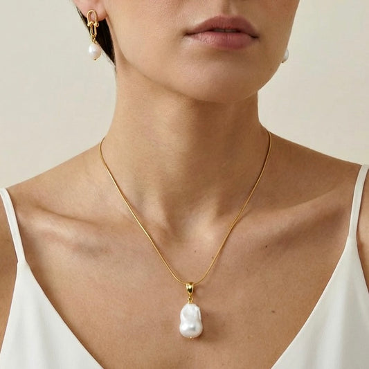 Woman wearing a gold necklace with a pearl pendant and matching earrings.