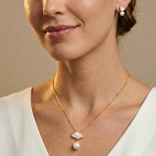 Close-up of a woman wearing a gold necklace with a pearl pendant and matching earrings.