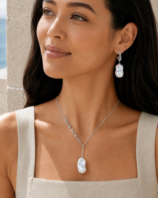 A woman wearing a silver necklace with a large white baroque pearl pendant and matching drop earrings