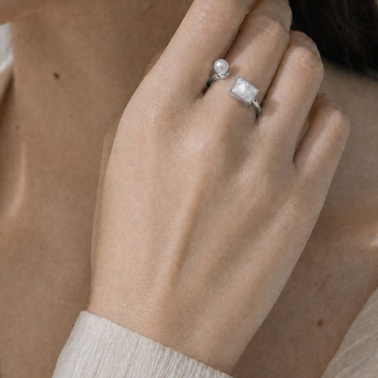 Close-up of a hand wearing a pearl ring with a neutral background
