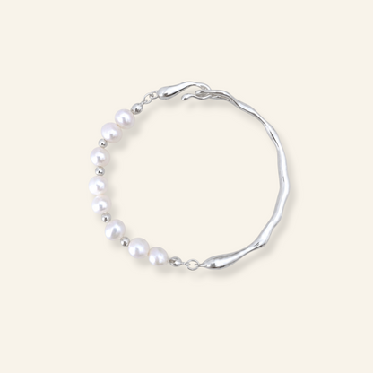 A silver-toned wavy bracelet featuring a curved row of white freshwater pearls, displayed on a solid light beige background.