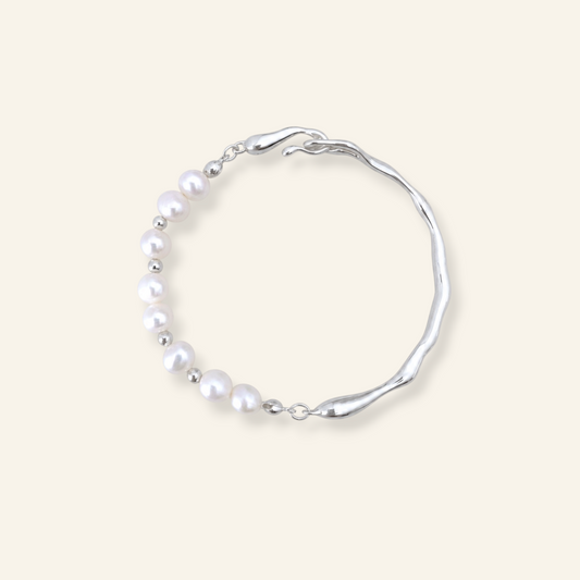 A silver-toned wavy bracelet featuring a curved row of white freshwater pearls, displayed on a solid light beige background.