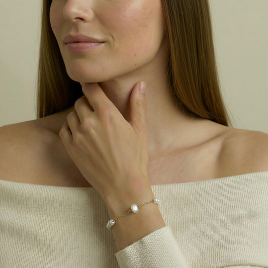Woman wearing a delicate bracelet with  pearl on a neutral background