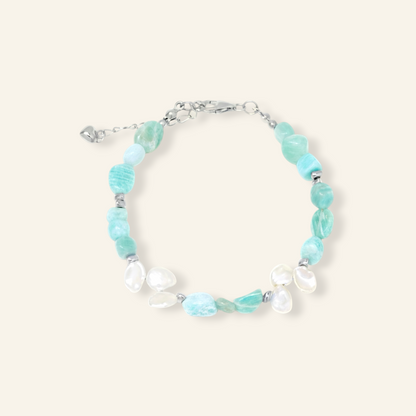 A delicate bracelet featuring light blue-green raw gemstone beads and white baroque shell beads, accented with small silver spacer beads and a silver chain clasp, shown on a solid cream background.