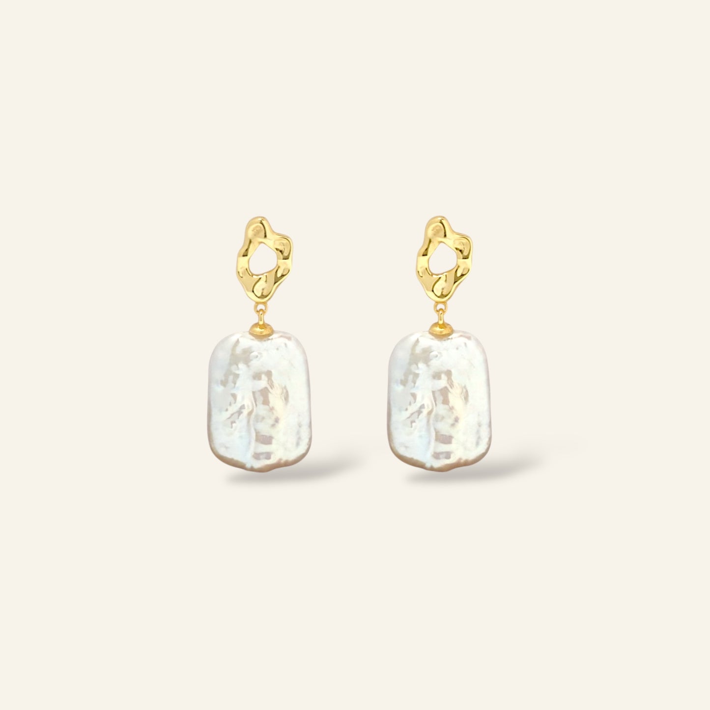 Gold earrings with white pearl drops on a light beige background