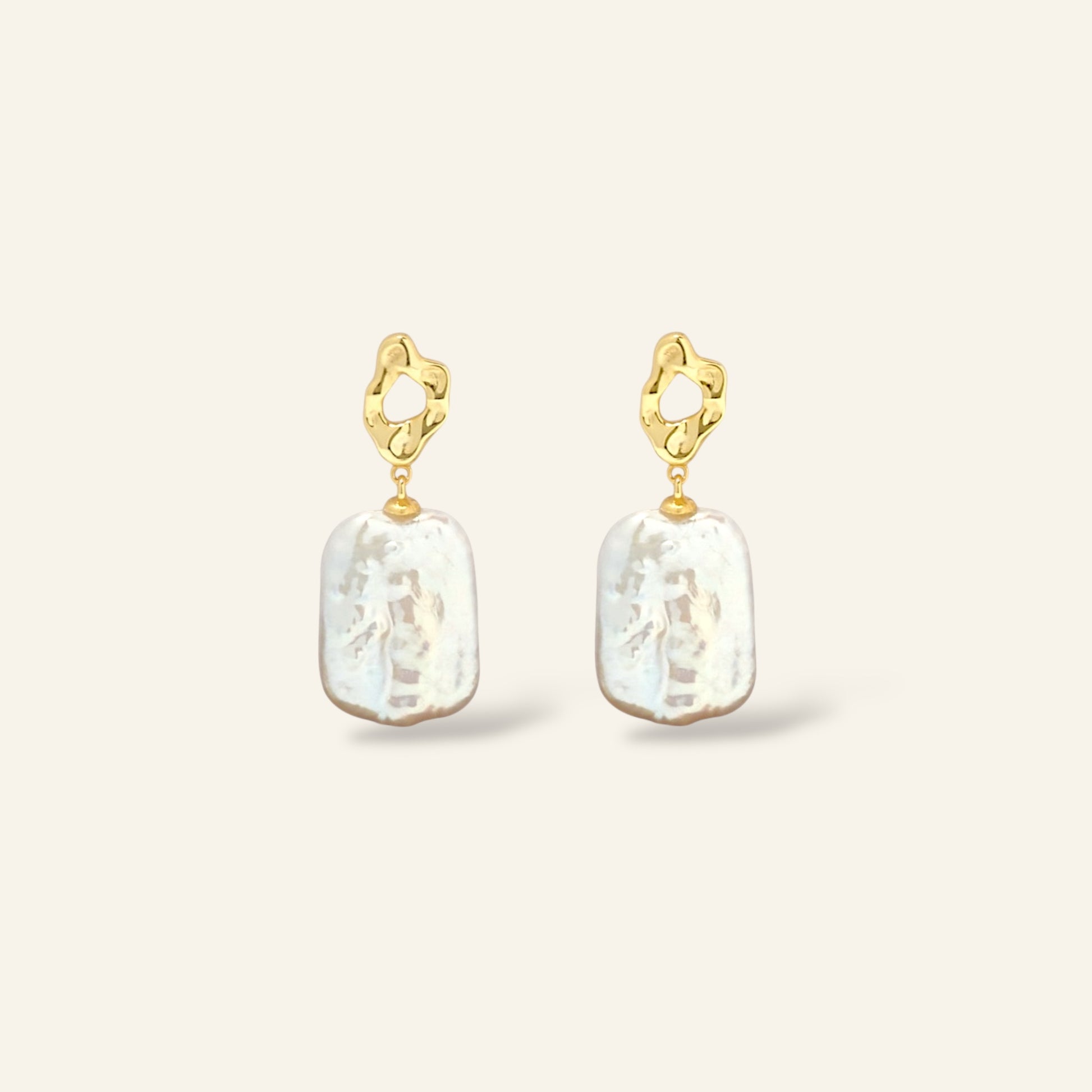 Gold earrings with white pearl drops on a light beige background