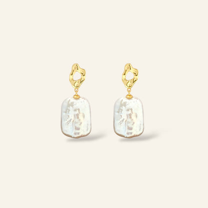 Gold earrings with white pearl drops on a light beige background