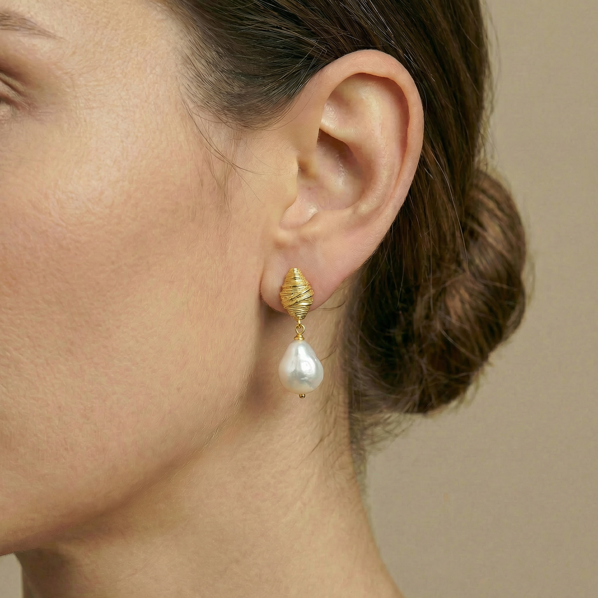 Close-up of a woman's ear wearing a gold earring with a pearl drop.