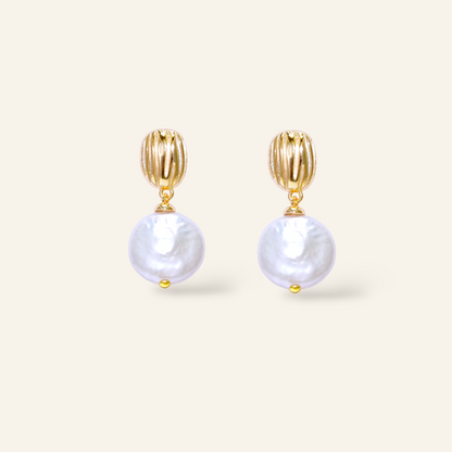 Gold earrings with pearl drops on a light beige background