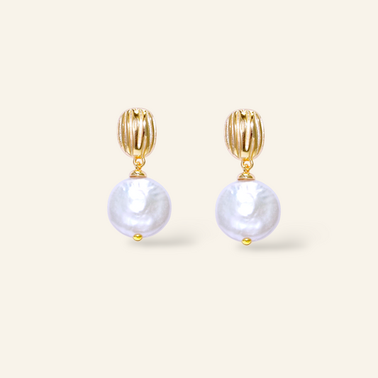 Gold earrings with pearl drops on a light beige background