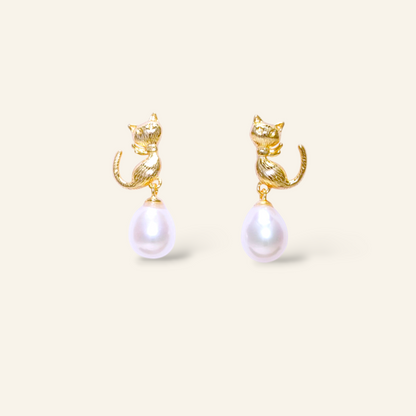 Gold cat-shaped earrings with pearl drops on a beige background