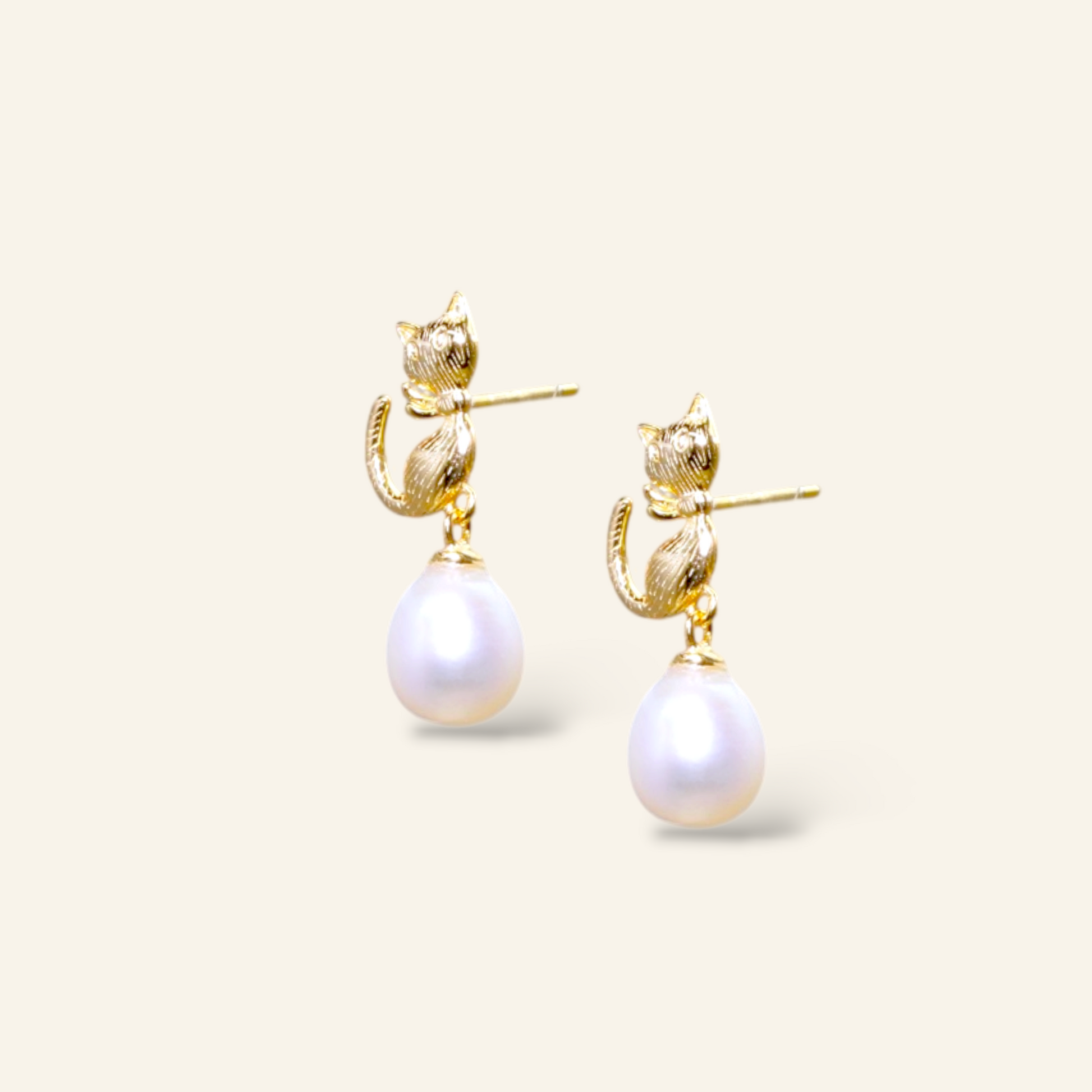 Gold earrings with pearl drops on a light beige background