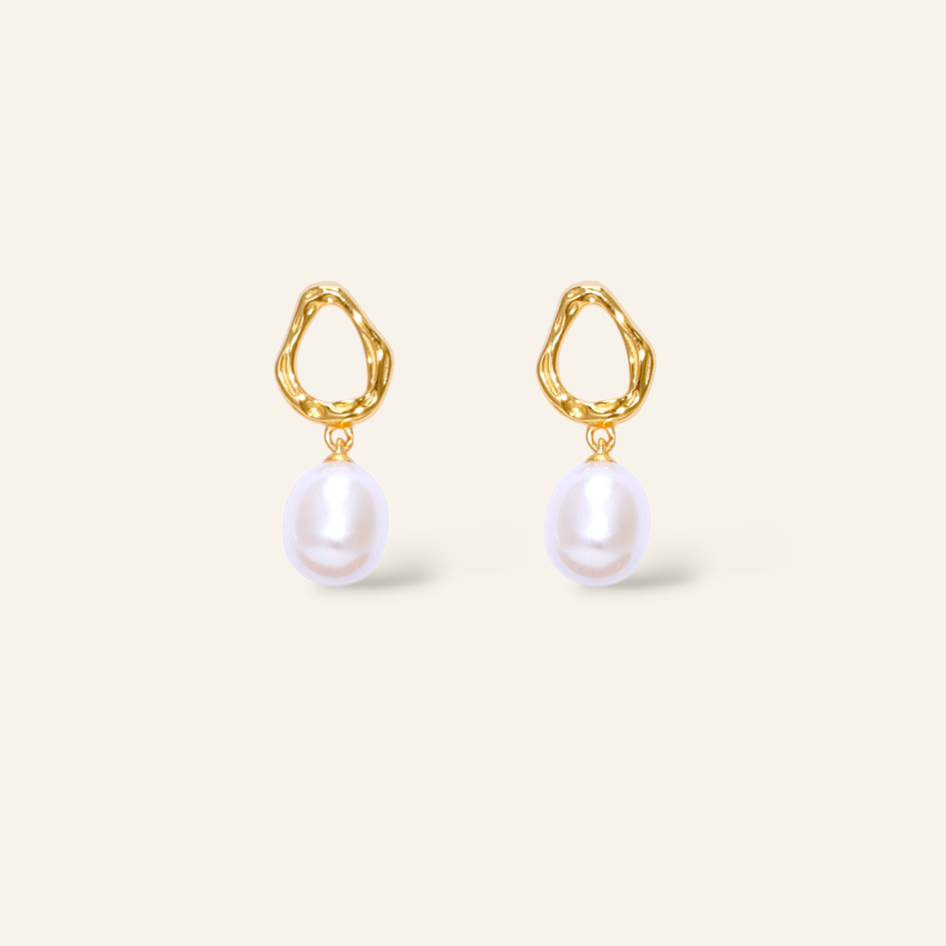 Gold earrings with pearl drops on a light beige background