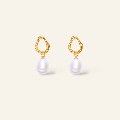 Gold earrings with pearl drops on a light beige background