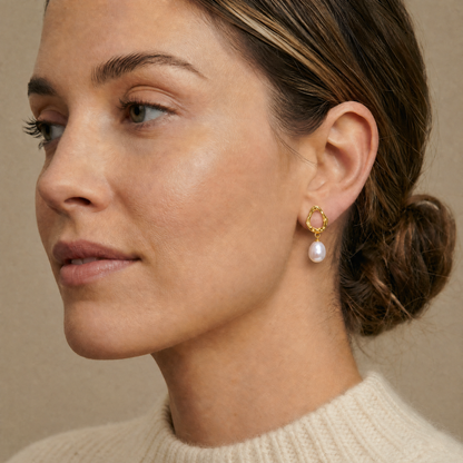 Close-up of a woman wearing a gold earring with a pearl on a beige background