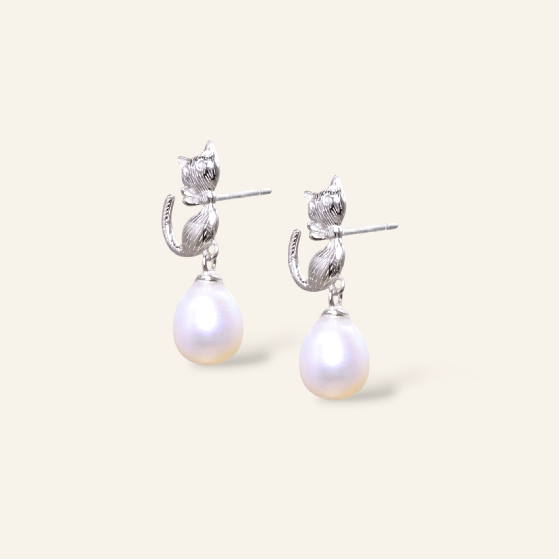 Pair of pearl earrings with silver cat-shaped clasps on a light beige background