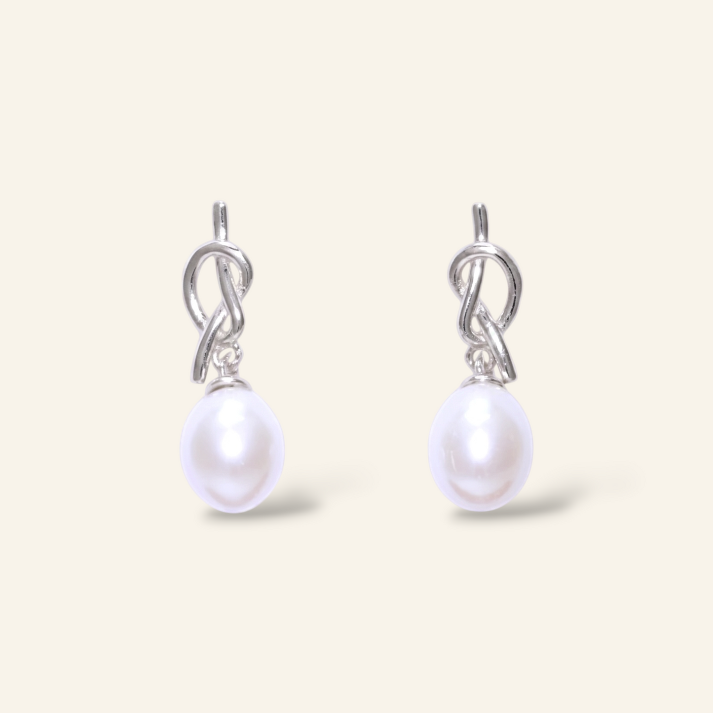 Pearl earrings with silver hooks on a light beige background