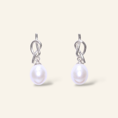 Pearl earrings with silver hooks on a light beige background