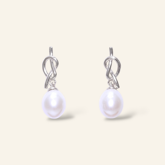 Pearl earrings with silver hooks on a light beige background