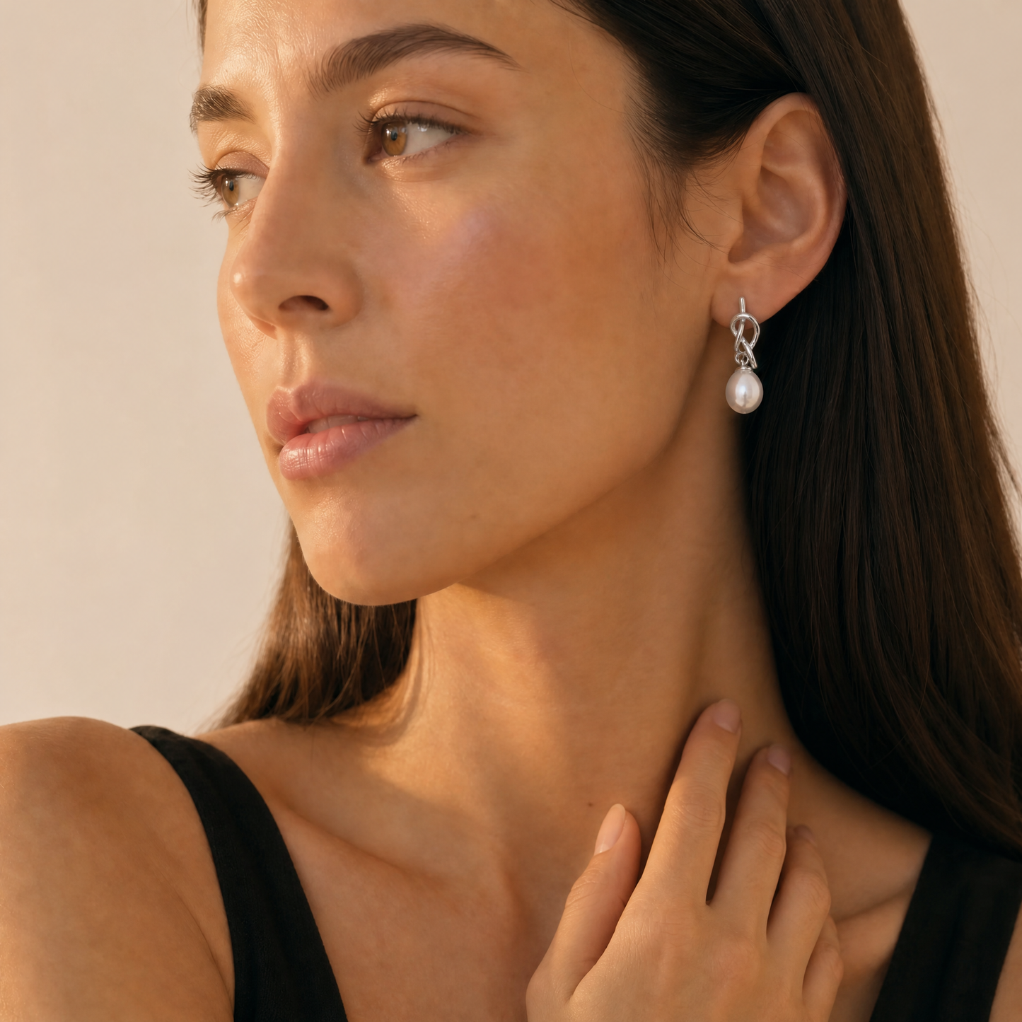 Close-up of a woman wearing pearl earrings with a neutral background