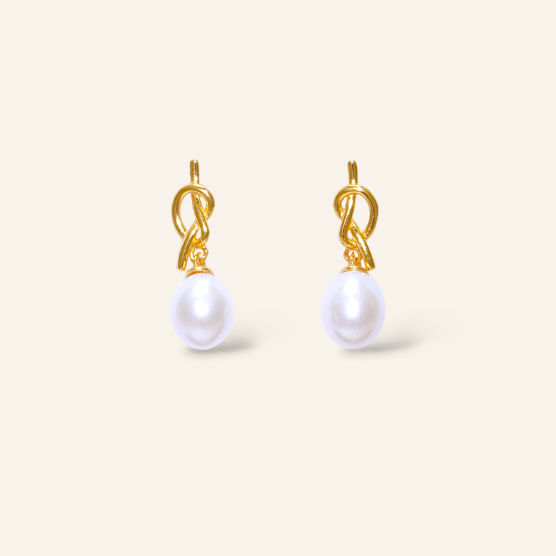 Pair of gold earrings with white pearls on a light beige background