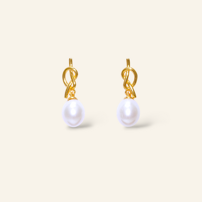 Pair of gold earrings with white pearls on a light beige background