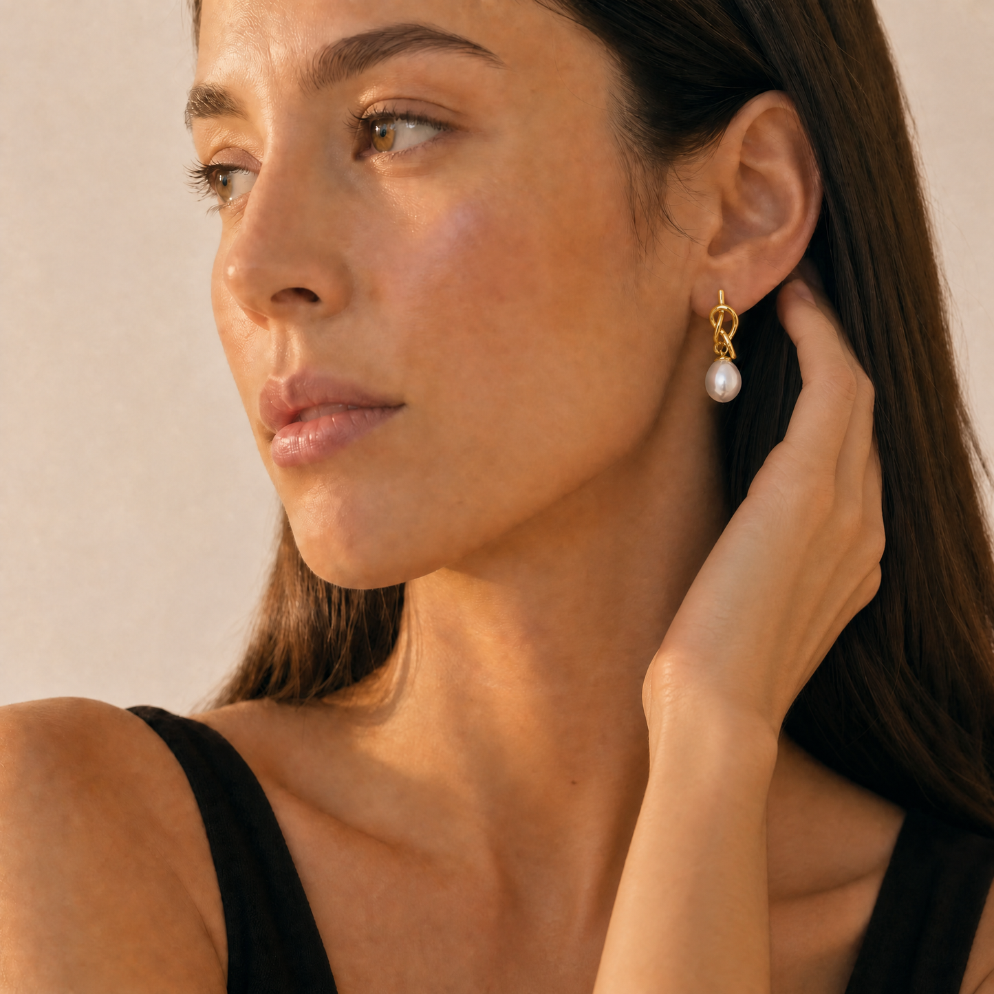 Woman wearing a gold earring with a pearl, against a neutral background