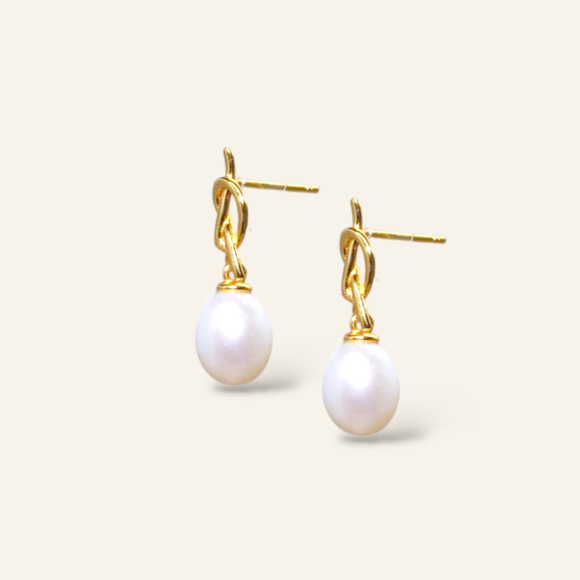 Pair of pearl earrings with gold hooks on a light beige background