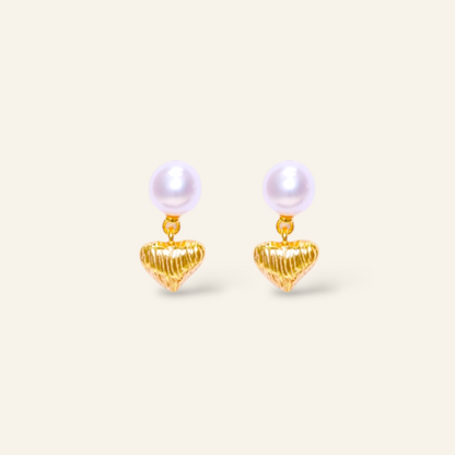 Pair of pearl earrings with gold heart-shaped drops on a light beige background