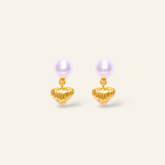 Pair of pearl earrings with gold heart-shaped drops on a light beige background