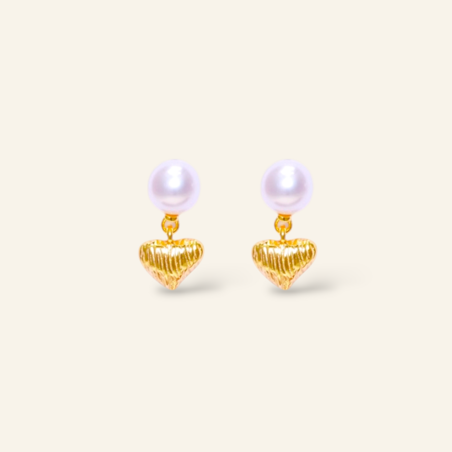 Pair of pearl earrings with gold heart-shaped drops on a light beige background