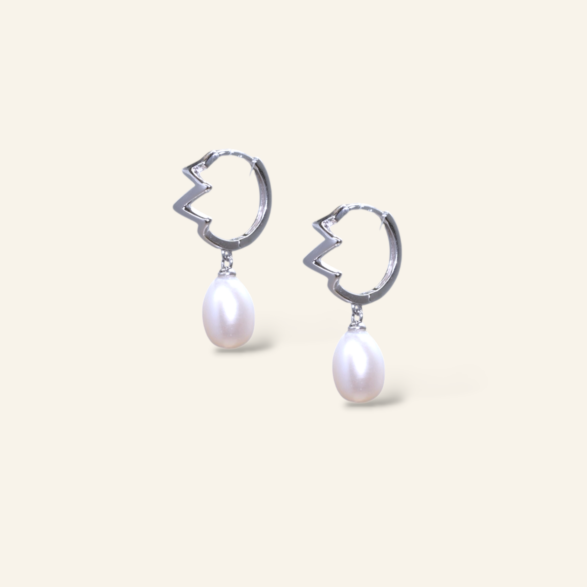 Pair of silver earrings with pearl drops on a light beige background