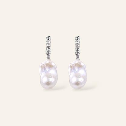 A pair of silver dangle earrings featuring irregular, lustrous white baroque pearls suspended from textured silver hooks