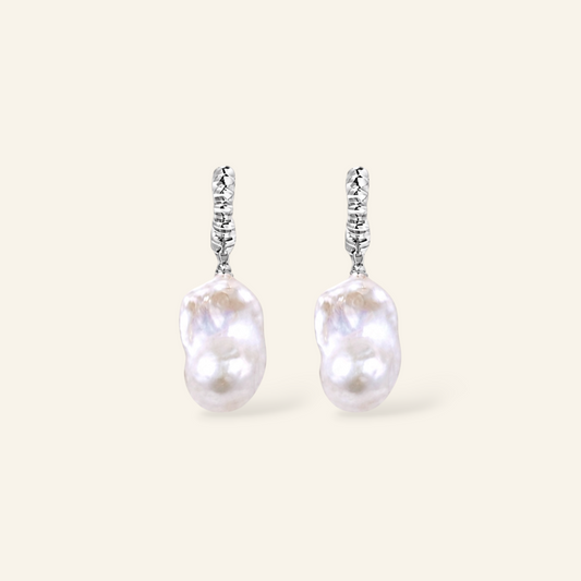 A pair of silver dangle earrings featuring irregular, lustrous white baroque pearls suspended from textured silver hooks