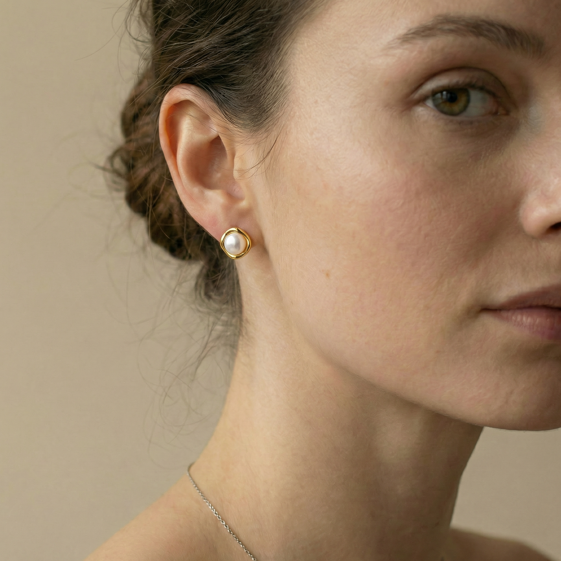 Close-up of a woman wearing gold earrings with a neutral background
