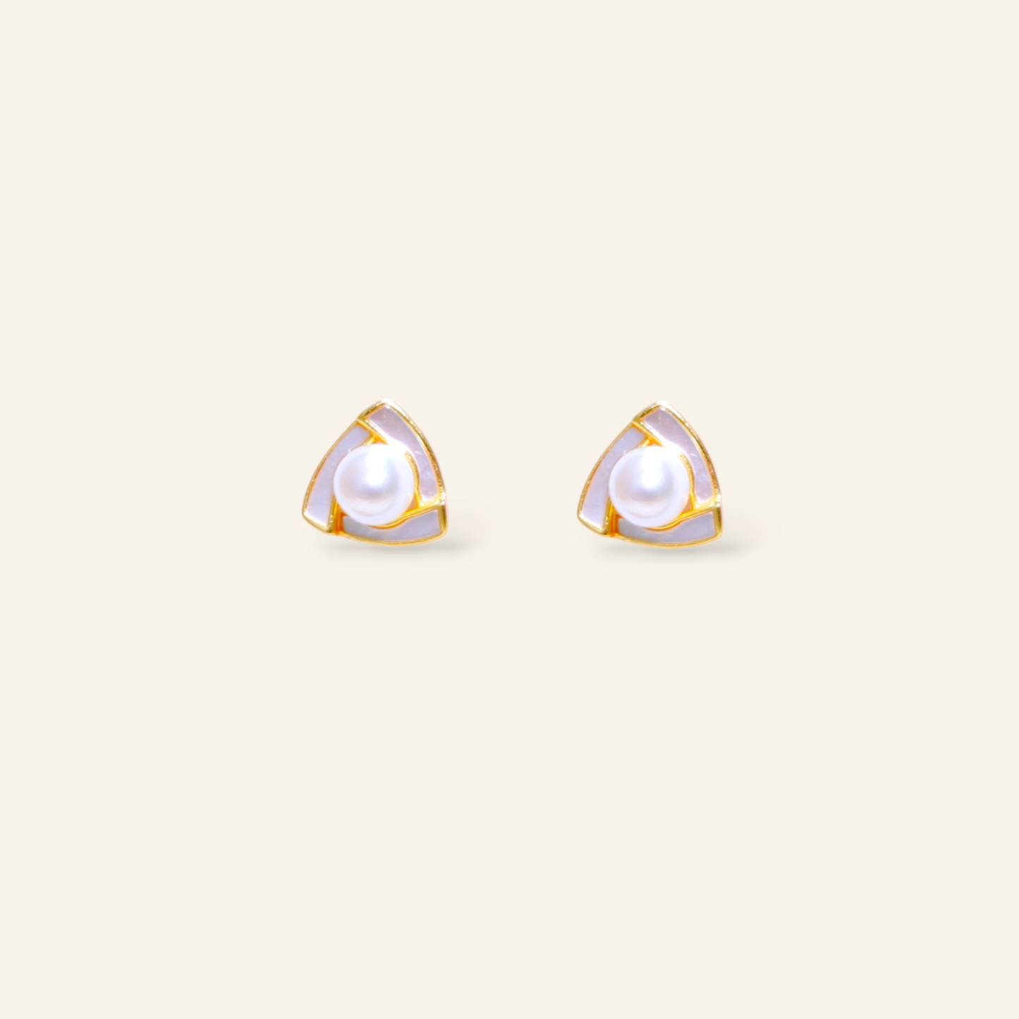 Pair of gold-trimmed pearl stud earrings on a light beige background