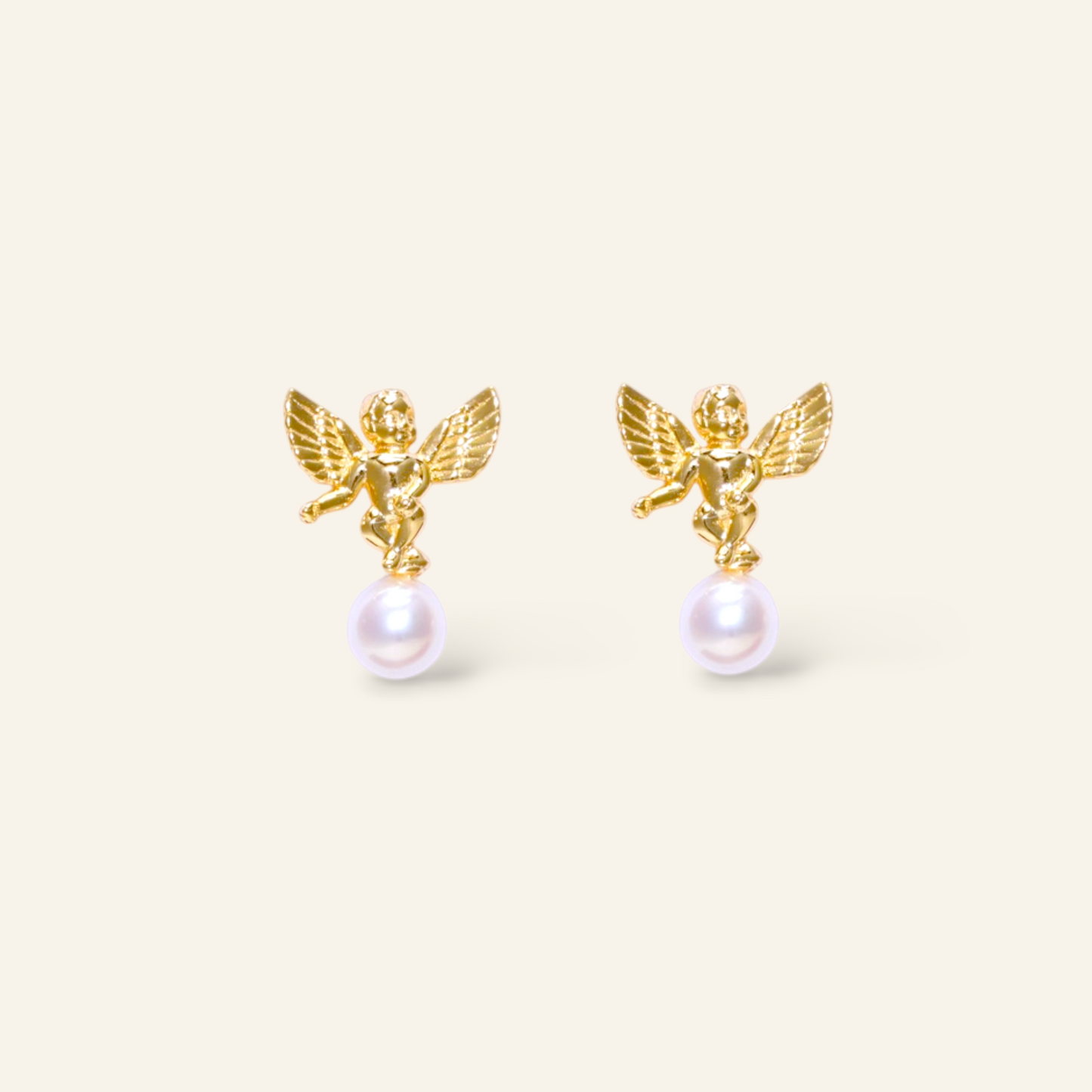 Gold angel earrings with pearl drops on a beige background