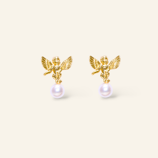 Gold angel earrings with pearl drops on a beige background