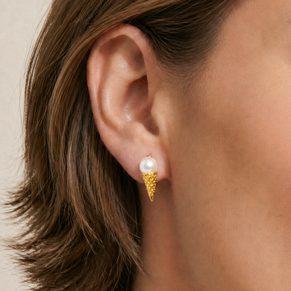 Close-up of an ear wearing a gold earring with a pearl