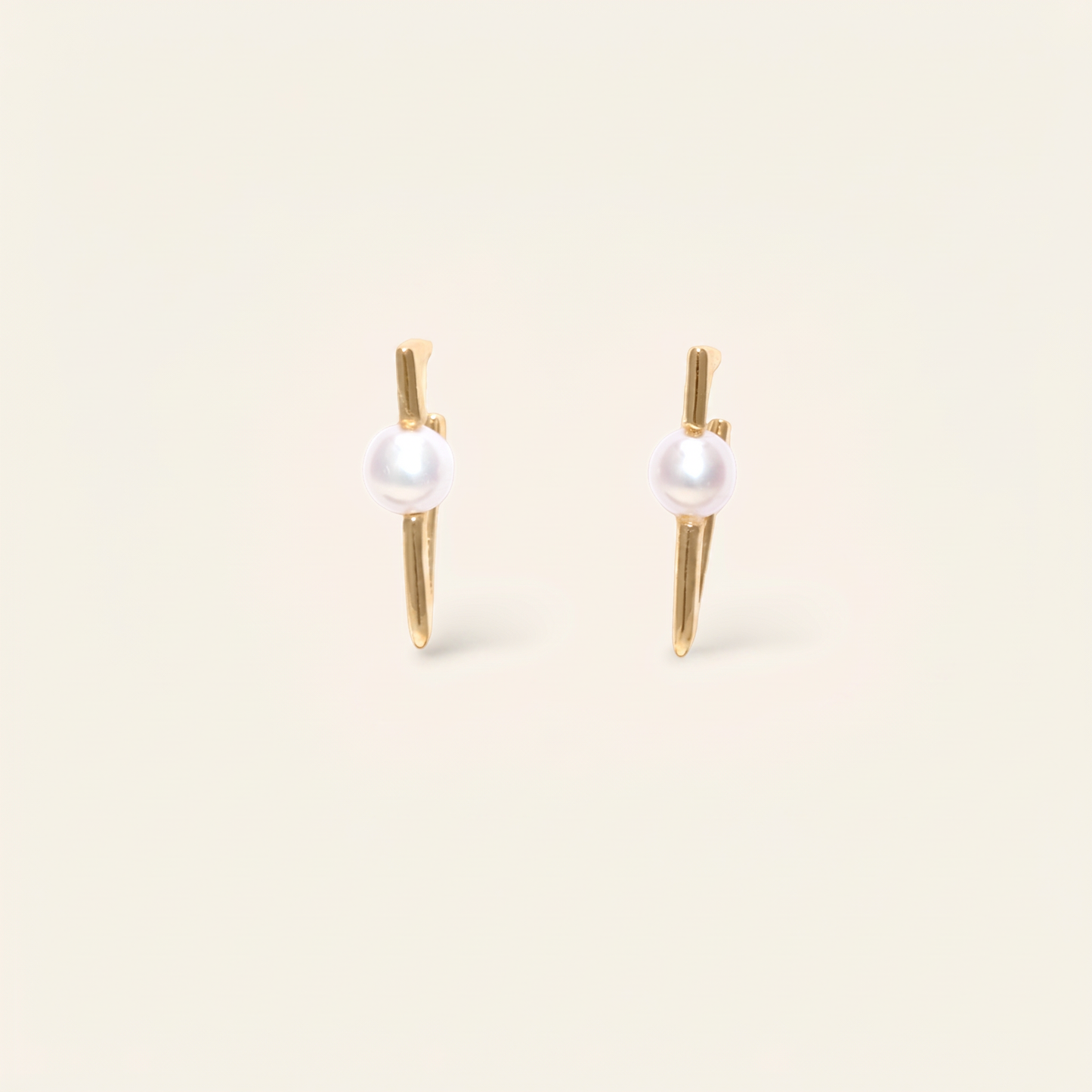 Pair of pearl earrings with gold posts on a beige background