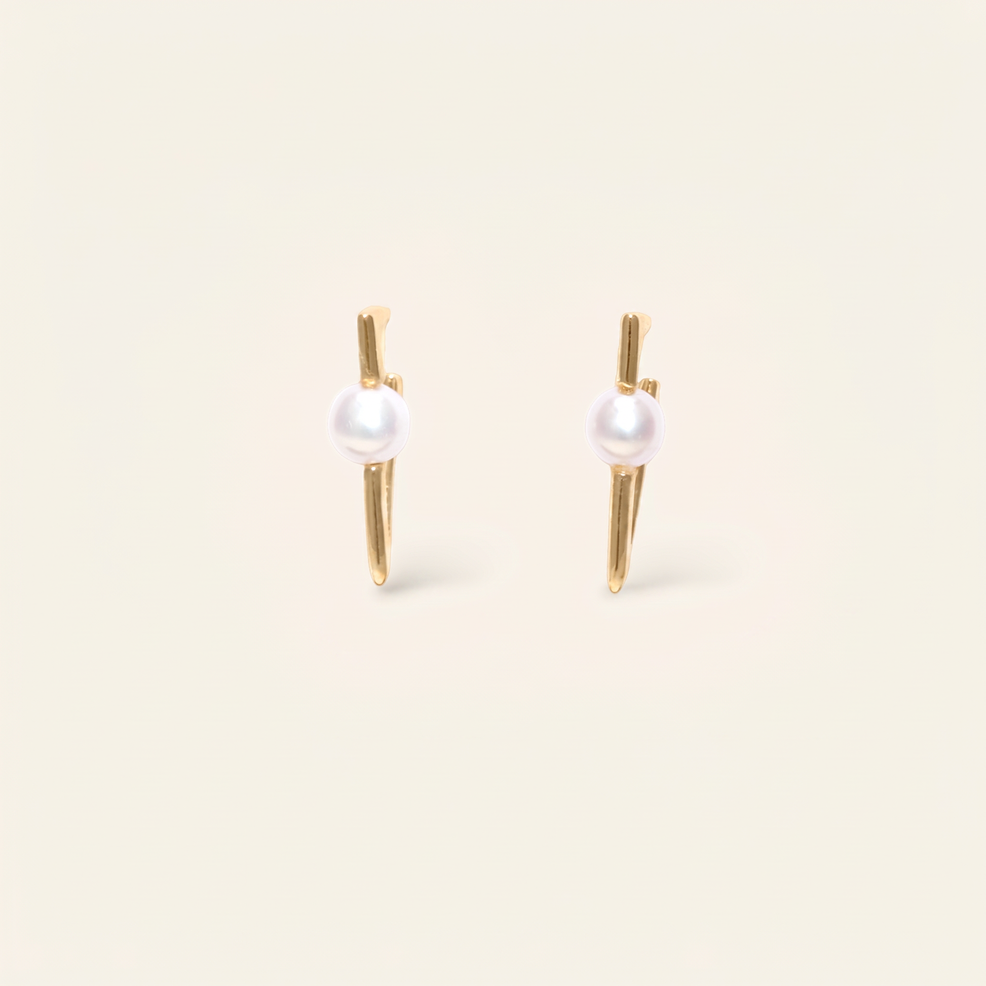 Pair of pearl earrings with gold posts on a beige background
