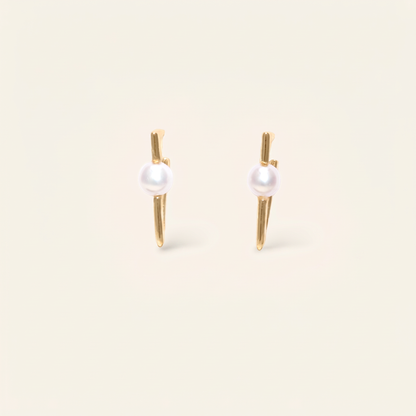 Pair of pearl earrings with gold posts on a beige background