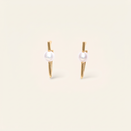 Pair of pearl earrings with gold posts on a beige background