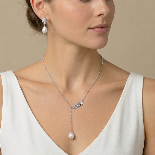 Model wearing a delicate freshwater pearl pendant necklace with a feather-inspired metal detail and a single white pearl.
