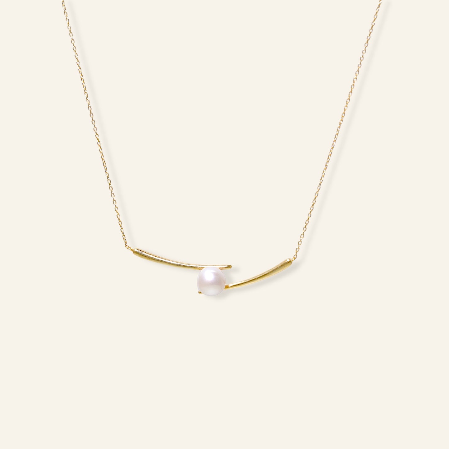 Gold necklace with a single pearl on a white background